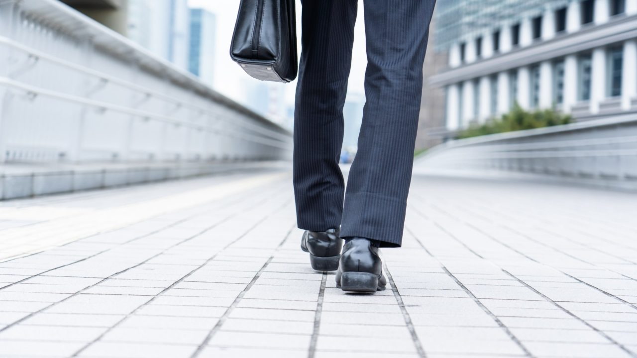 歩いているスーツ姿の男性の後ろ姿の足元